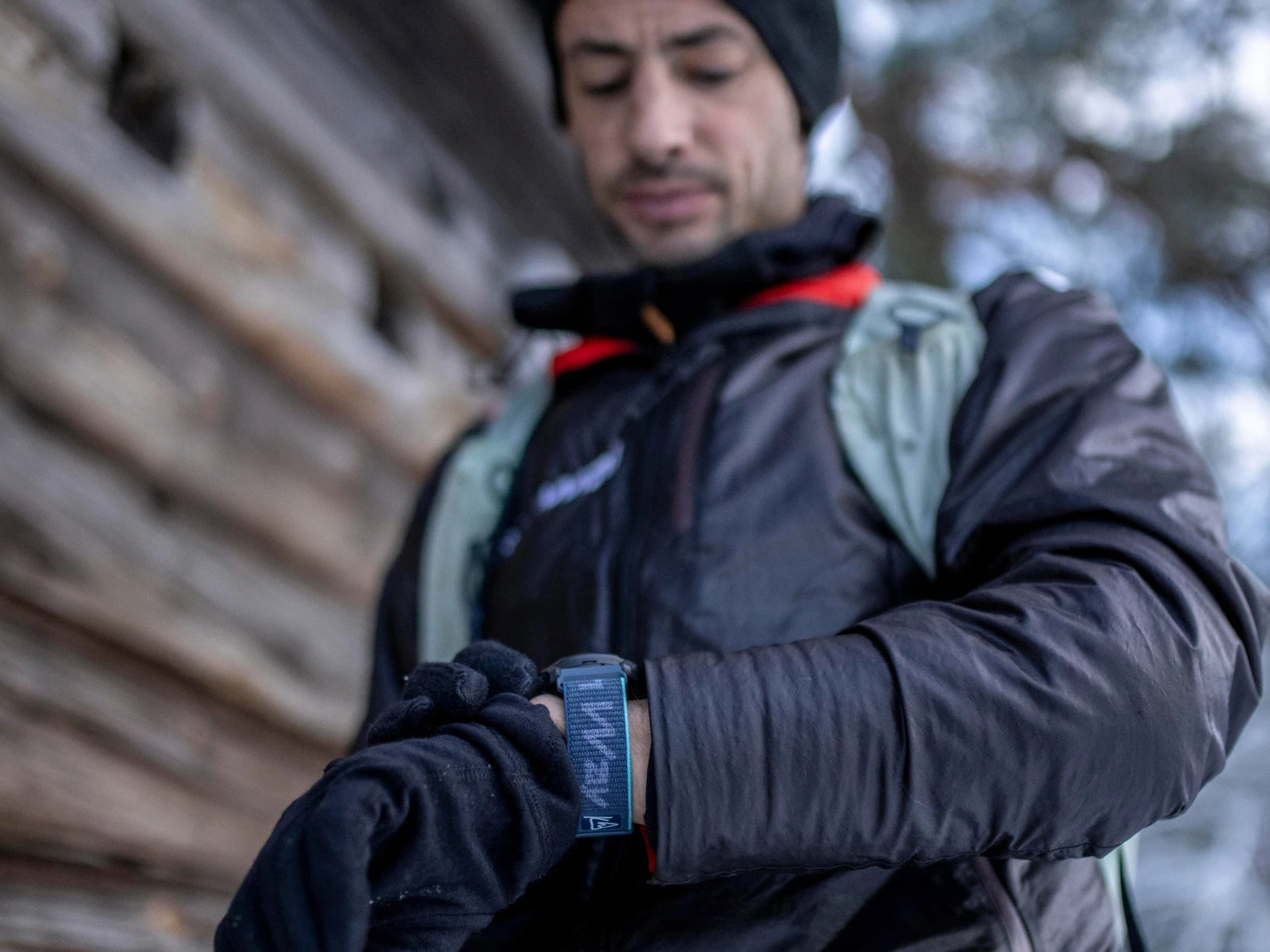 Kilian Jornet wearing a black jacket and gloves, looking at his blue outdoor GPS-watch outdoors.